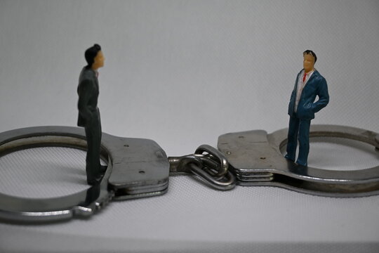 Two small professional figures positioned inside handcuff rings symbolizing corporate dispute or legal entrapment