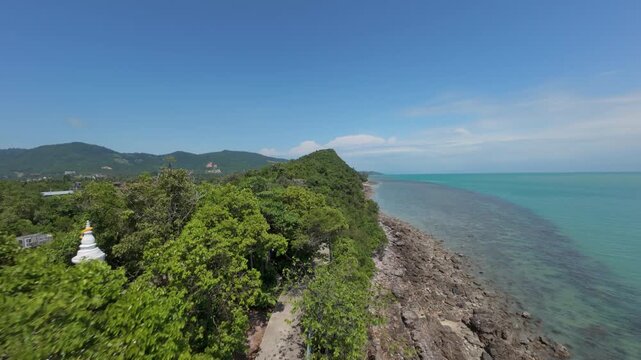 Aerial View of Tropical Road Winding Along Rocky Shoreline with Dense Green Foliage and Clear Turquoise Sea for Scenic Eco Travel Concept
