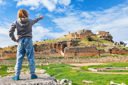 Young child looks at acropolis of ancient Greek city Tlos in Lycia located on Lycian way. Famous historical site In Antalya region. Popular place for family travel on summer vacation. Fethiye, Turkey