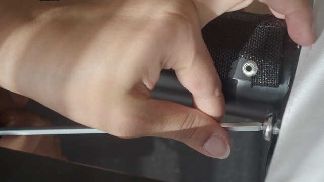 Person tightening bolt on black furniture frame with metal allen key tool in close up view.