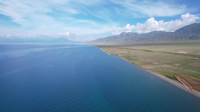 Stunning aerial time-lapse of Sayram Lake in Xinjiang with snow mountains, grassland, river, and highway, showcasing breathtaking natural beauty.