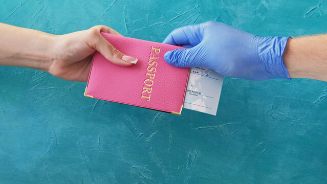 Flight check-in. Quarantine travel. Customs officer hand in protective glove giving pink passport ticket to female passenger on blue.
