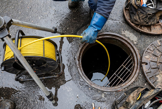 Plumber using a flexible inspection camera to examine a sewer line through an open manhole