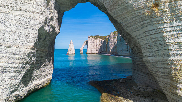 Framed perspective of the Needle and Aval Arch through the massive Manneporte natural arch in Etretat, Normandy, France