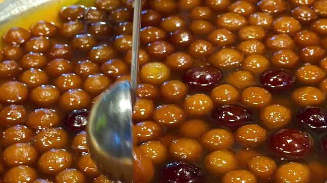 Close up of traditional indian sweet gulab jamun being dipped in warm sugar syrup