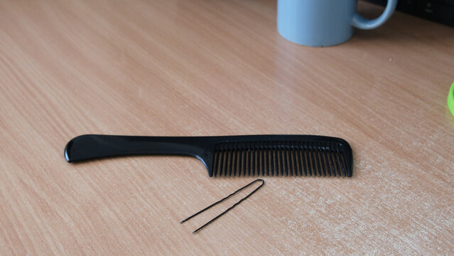 Black plastic comb and hairpin lying on light wooden table .