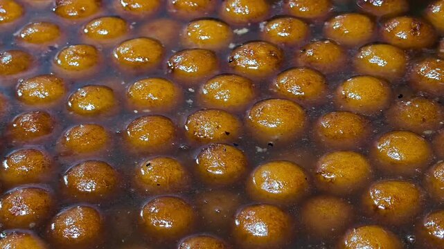 Close up of traditional indian sweet gulab jamun being dipped in warm sugar syrup