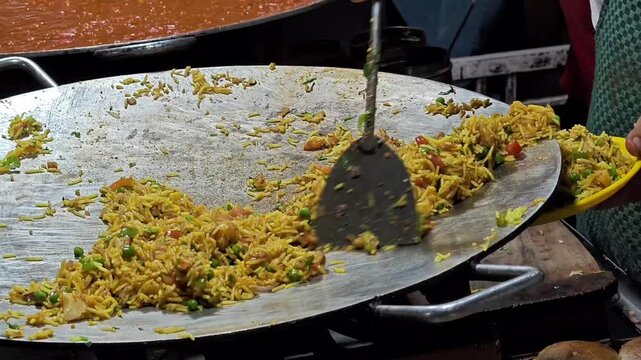 Street vendor stirring spicy tawa pulav fried rice with vegetables on a large flat pan
