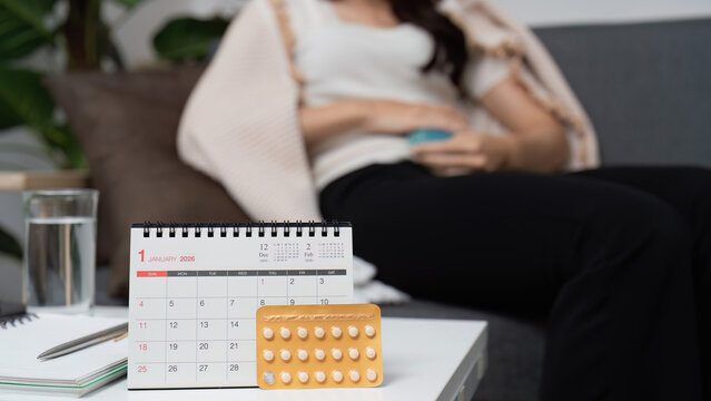Birth control pills and calendar on table with woman in background