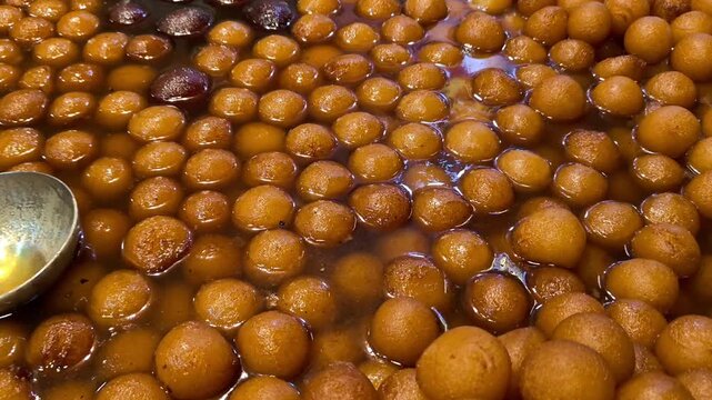 Close up of traditional indian sweet gulab jamun being dipped in warm sugar syrup