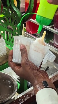 Street food vendor pouring colorful syrup over crushed ice gola in plastic cups