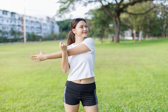 Young woman stretching arm, exercising outdoors in park