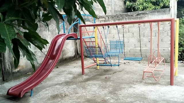 A colorful playground with a red slide and swings in a outdoor setting with trees and a concrete wall in the background video