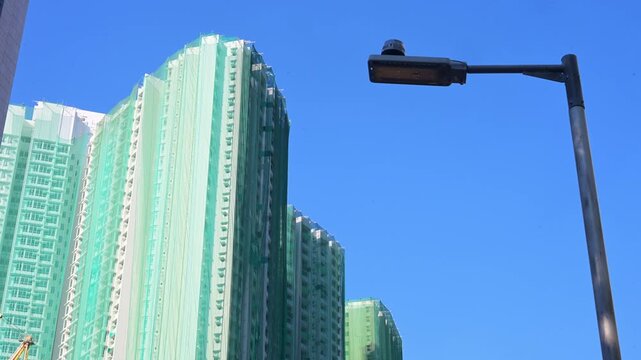 Residential skyscrapers undergo renovation covered in green protective netting in Hong Kong. Establishing shot of urban renewal, building maintenance, and real estate development in China.
