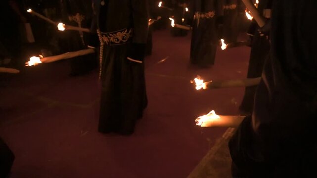 Crowd of people in black robes carrying burning torches during a night religious parade
