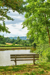 Lake, park and bench with trees for landscape, outdoor and clouds with sky in springtime. Seat,...