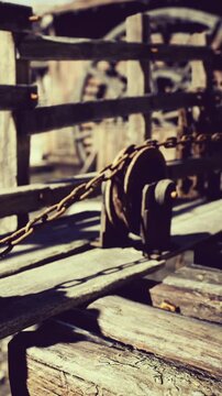 A beautifully crafted wooden pulley rests on a weathered deck, surrounded by peaceful nature. Sunlight filters through trees, casting intricate shadows on the scene.
