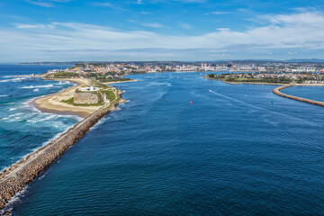 Obraz premium Aerial drone view of Nobbys Lighthouse and sandy Nobbys Beach with Newcastle city skyline and working harbour in the background.
