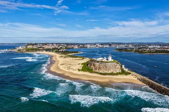 Aerial drone view of Nobbys Lighthouse and sandy Nobbys Beach with Newcastle city skyline and working harbour in the background.
