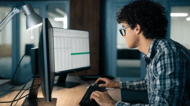 Medium shot of analyst concentrating on dual monitors displaying real estate loan spreadsheets focusing on property valuation and risk assessment during commercial underwriting