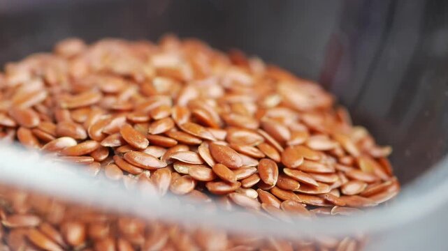 Close up view of raw flax seeds spilling into clear bowl, healthy food ingredient.