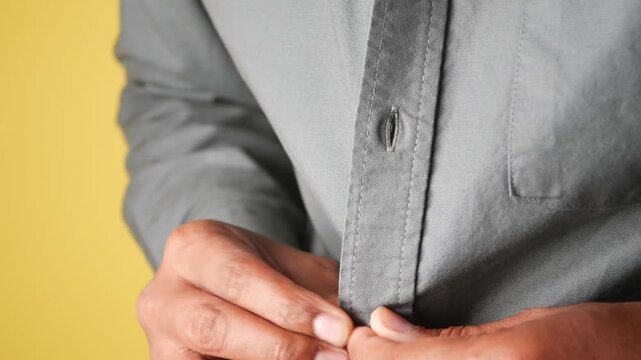 Man buttons up gray shirt in close-up motion, getting dressed for work.