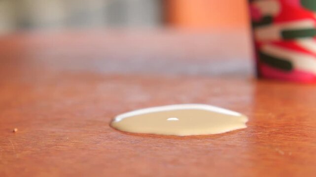 Slow motion spill of coffee with cream on wooden surface with colorful cup in background.