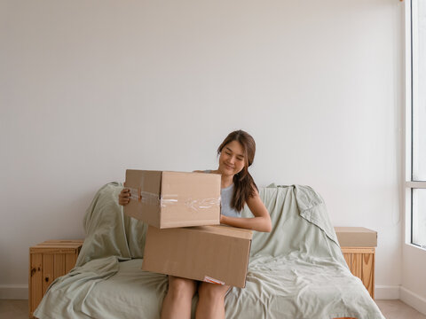 Asian woman balancing cardboard boxes while seated on bed in white shirt and clean background