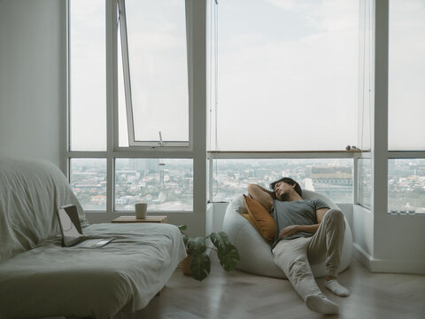 Asian man sitting on the bean bag at the balcony of the condominium, feeling bored and lonely.
