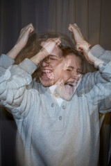 Vertical of Caucasian young adult woman expressing intense emotion with hands raised and face contorted in anguish, double exposure effect emphasizing psychological distress