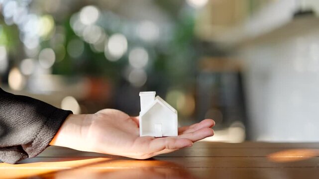 Small white house model on human hand with natural bokeh background, real estate investment and home ownership concept, property insurance and mortgage loan protection.