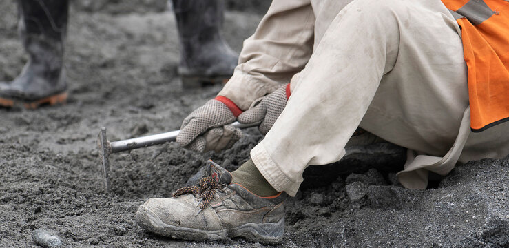 Construction worker collecting soil sample with hand tool in field work close-up.