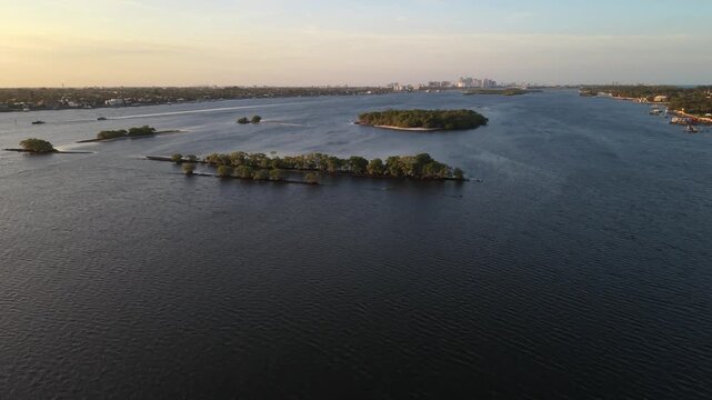 Drone near Summa Beach Park and S. Flagler Dr. at golden hour flying north toward Hunters Island in the ICW, Intracoastal Waterway with West Palm Beach in the distance and boats on the water.