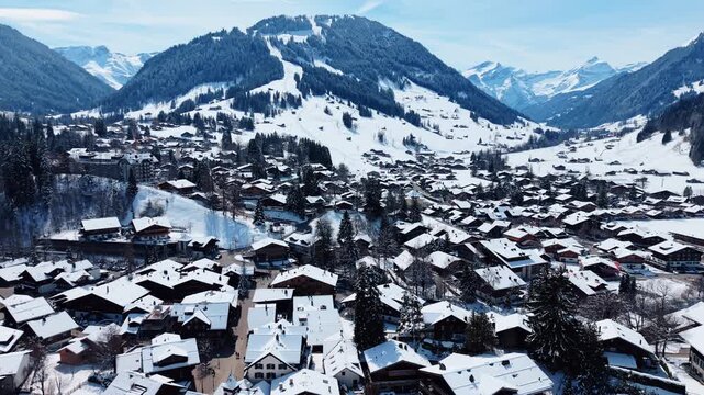 Aerial: townscape of Gstaad with snow in winter during the day in Canton of Bern, Switzerland, pull out drone shot