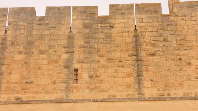 Close-up view of ancient fortification wall with crenellations in Aigues-Mortes, France. Medieval stone architecture showcasing historic defensive ramparts and castle battlements.