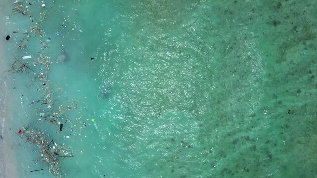 Ocean water showing a sea turtle swimming near the shore and accumulating plastic waste, highlighting environmental pollution impact. Smooth aerial view vertical bird's eye view drone