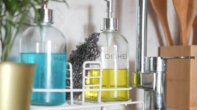 Dish soap and hand soap dispensers with steel wool in kitchen, close up shot with motion.