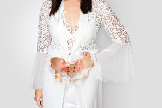 Pregnant woman in white satin nightwear holding lower abdomen due to pelvic pain, inflammation, or pregnancy discomfort isolated on white background