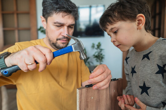 Father teaching son to assemble furniture at home with hammer