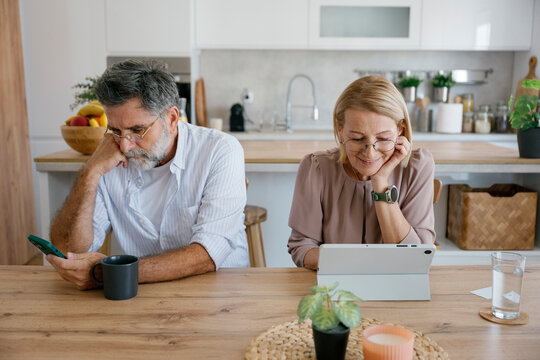 Married couple sitting at home using digital tablet and smartphone