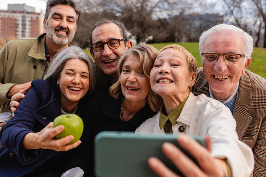 A group of diverse elderly people taking a selfie together in a park, enjoying their time and smiling.