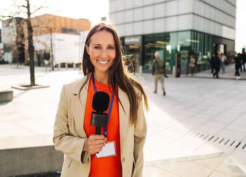 Smiling reporter with microphone conducting interview outdoors