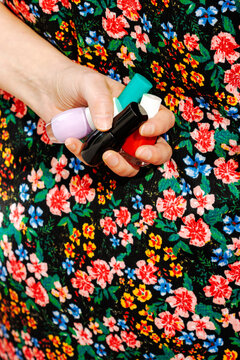 Hand holding colorful nail polish bottles against floral spring dress