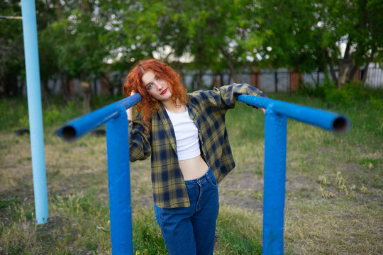 Red haired woman in jeans relaxing at old playground on parallel bars