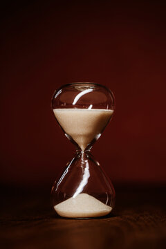 Hourglass with sand on wooden surface against warm red background