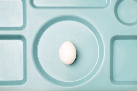 White egg on blue tray with geometric minimalist composition