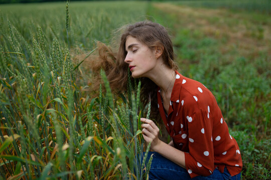 Woman in red polka-dot blouse kneeling in summer wheat field