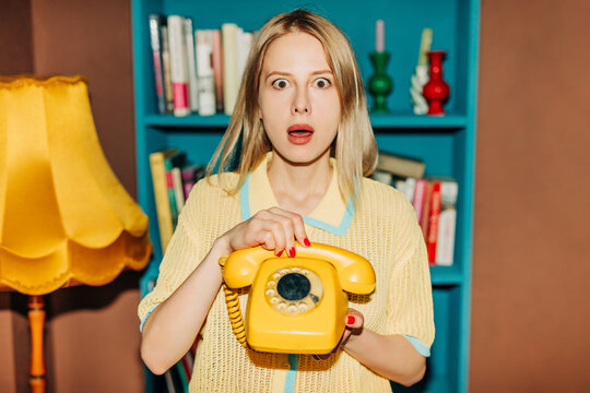 Surprised woman holding retro yellow telephone indoors