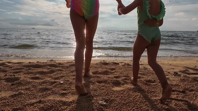 Two young girls holding hands and playing at the beach shoreline during sunset