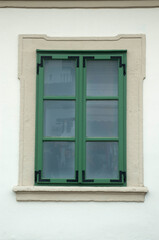 Fototapeta premium Green wooden window with decorative wrought Iron reinforcement brackets and ecru frame on white wall
